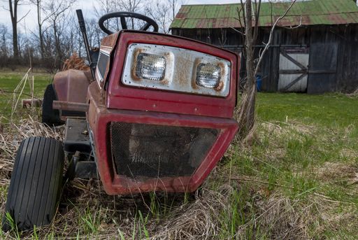 A closeup shot of an old red tractor in a garden by a house captured on a sunny day