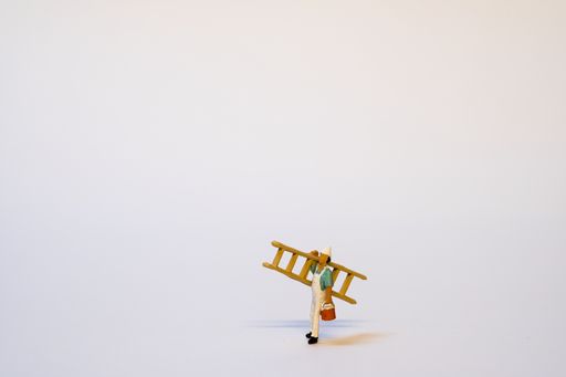 A small miniature painter in work clothes carrying a wooden ladder, on a white background