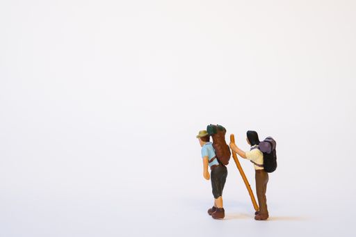 Two miniature mountain hikers with backpack and walking sticks on a white background, copy space