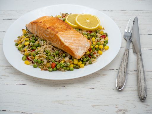 A plate with meal of vegetables, rice, salmon and lemon slices