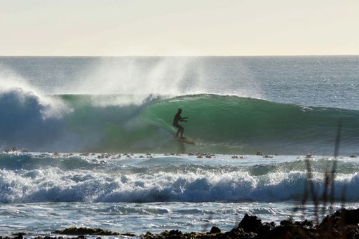 A scenic shot of a person surfing through the waves of the ocean on a sunny day