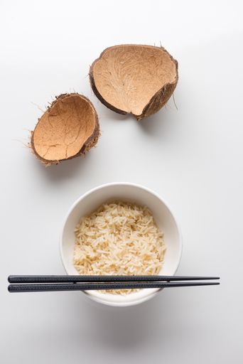 A closeup shot of cooked rice in a white plastic bowl with chopsticks on it on a white background