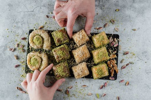 A closeup of male and female hands taking delicious baklavas from a black cutting board