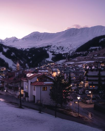 A vertical shot of dense buildings with illuminated lights and mountains under a clear sky in winter
