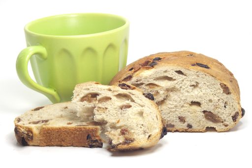 A beautiful closeup of a donut bread with raisins grapes next to the green cup