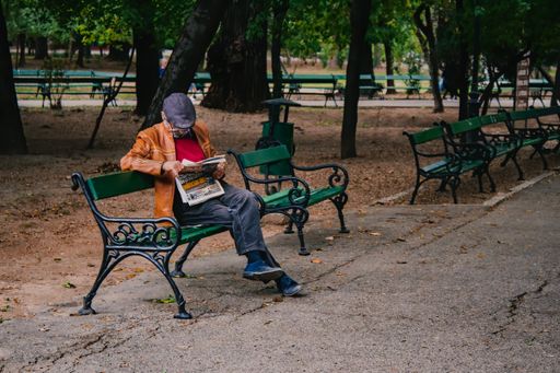 An old grandfather sitting on the bench and reading a newspaper