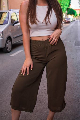A vertical shot of a lady wearing a white top with summer pants posing on the street