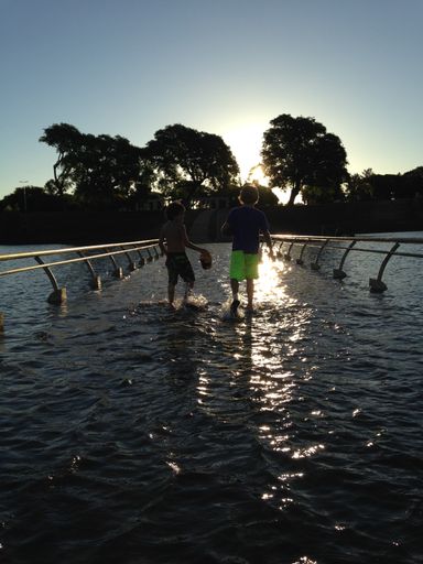 A vertical shot of two young boys walking on water surrounded by trees during sunset