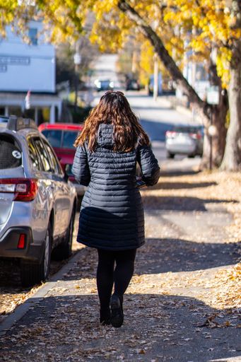 A vertical shot of a woman with coat walking down street in a sunny day