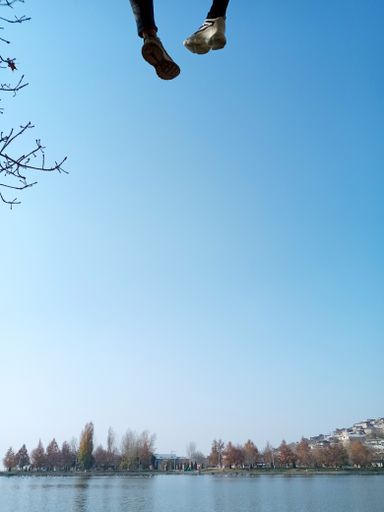 A vertical shot of a lake and feet hanging on the top with the trees in the background