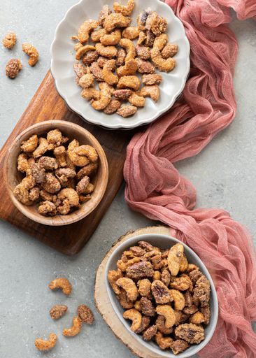 A top view of candied cashew nuts in plates on wooden board near the pink scarf
