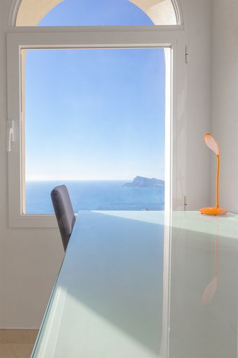 The interior with modern white table, a chair and a lamp with a big window viewing the ocean