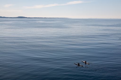 Two tourists kayaking on the open ocean under the sunlight