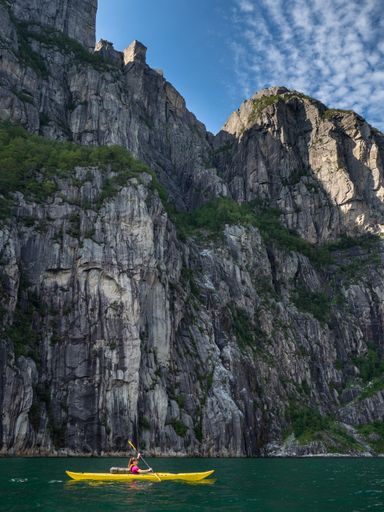 A vertical shot of a tourist kayaking on the Lysefjorden under the sunlight in Norway