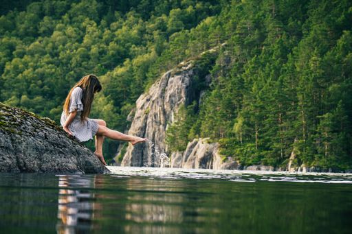 A young woman is dipping her feet in a mountain lake.