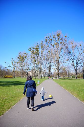 A vertical shot of a woman and a child walking with a ball on a footpath in the Jan Pawla park.