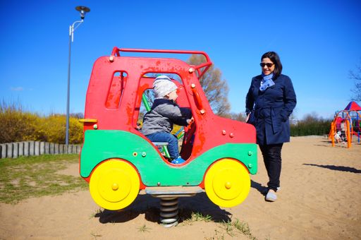 A woman watching a child sitting in a car-shaped spring swing in the Jan Pawla park.