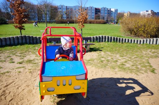 A young boy sitting in a car-shaped spring swing equipment on a sandy playground in the Jan Pawla park.