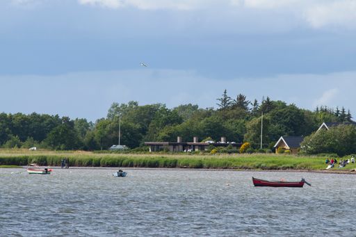 A beautiful view of a small boats in the sea with a big green land with trees and houses in Hals, Denmark