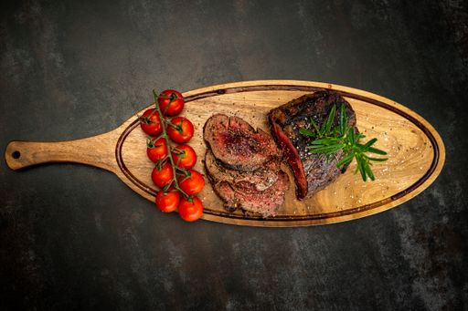 A medium cooked steak served with red cherries on a wooden board