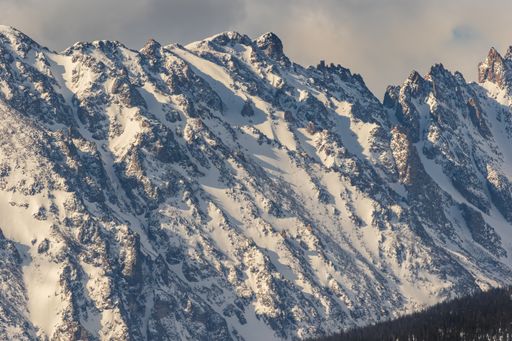 A closeup scenic view of a mountain chain covered with snow with forest on its slope