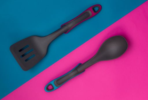 A top view of diagonally divided blue and pink sections with a kitchen scraper and a spoon on each