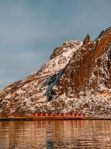 A vertical shot of houses on the lakeshore under the snowy rock