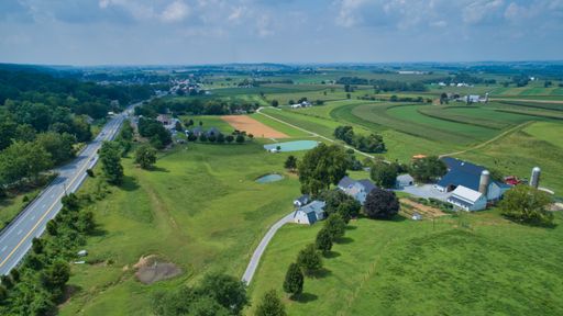 An aerial shot of a field and houses under a cloudy blue sky