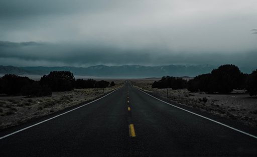 A traffic road passing through the fields with green bushes against a cloudy sky at sunset