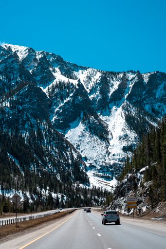 A mesmerizing view of high snowy hills over the traffic road along the dense growing trees