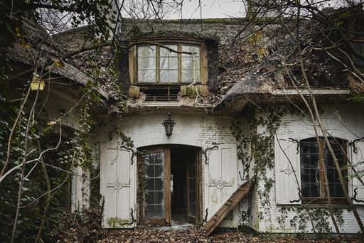 A horizontal shot of an abandoned white house with dry plants on it