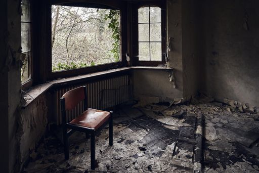 A horizontal shot of an abandoned room with a wide window and a chair in front of it