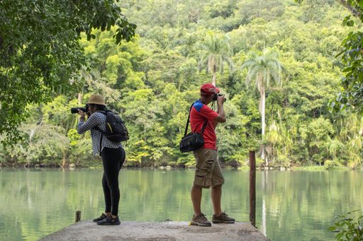 Two Hispanic tourists taking a picture of a beautiful lake with their digital cameras during