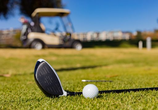 A closeup of a golf club and a ball on a golf course fairway on a sunny day
