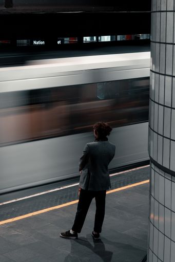 A back shot of a young female standing in front of a motion speed subway train  at night