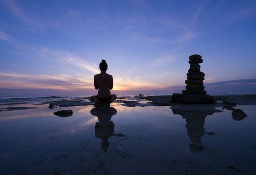 A closeup shot of a half-naked woman sitting near the water surface and doing yoga at sunset