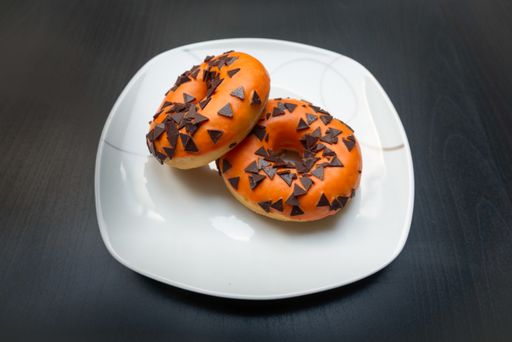 Two delicious halloween style donuts on white plate lying on black table with orange icing and brown chocolate decoration.