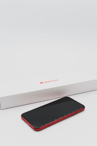 closed Apple watch product red box and iphone on a white tabletop with text space