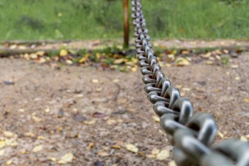 A selective focus shot of a metal chain hanging down a pole next to grass and fallen leaves