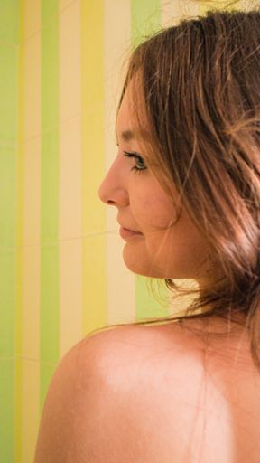 A vertical shot of a beautiful brunette female with a naked shoulder standing in the bathroom