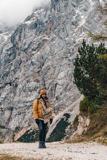 A vertical shot of a Caucasian female walking on a pathway under Mount Prisank covered with snow and fog in Slovenia