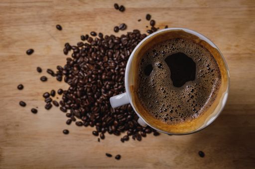 A top view of a cup of coffee and coffee beans on a wooden table