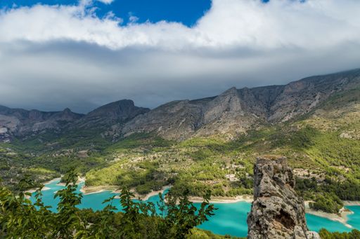 A scenery of a river surrounded by plants on a mountain range on a cloudy day