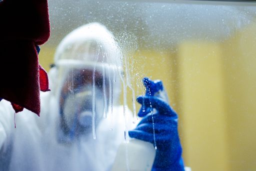 A closeup shot of an adult male wearing protective clothing disinfecting  the windows