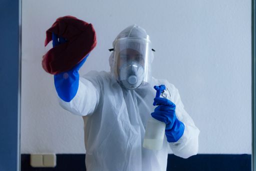 A closeup shot of an adult male wearing protective clothing disinfecting  the windows
