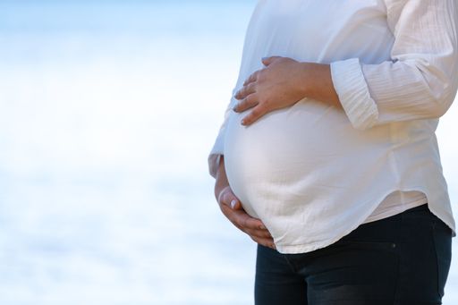 A pregnant woman in white t shirt stands in profile holding her hands on her stomach. Blurred, bokeh background with place for text, copy space.