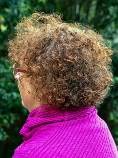 A side shot of a short hair curly woman with glasses wearing a purple sweater in the park