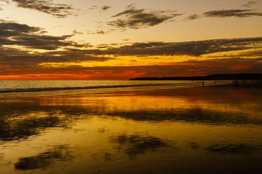 a Dramatic yellow orange sunset over the ocean with yellow rays reflected on the water and the small cloud pockets in the sky