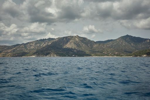 Mountain range seen from in the middle of the sea under a cloudy sky.