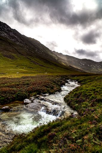 A vertical shot of the river in the valley surrounded by hills.